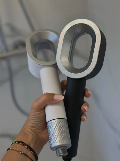 Image d’une main qui tient les deux pommeaux de douche filtrants blanc et noir, dans une salle de bain.